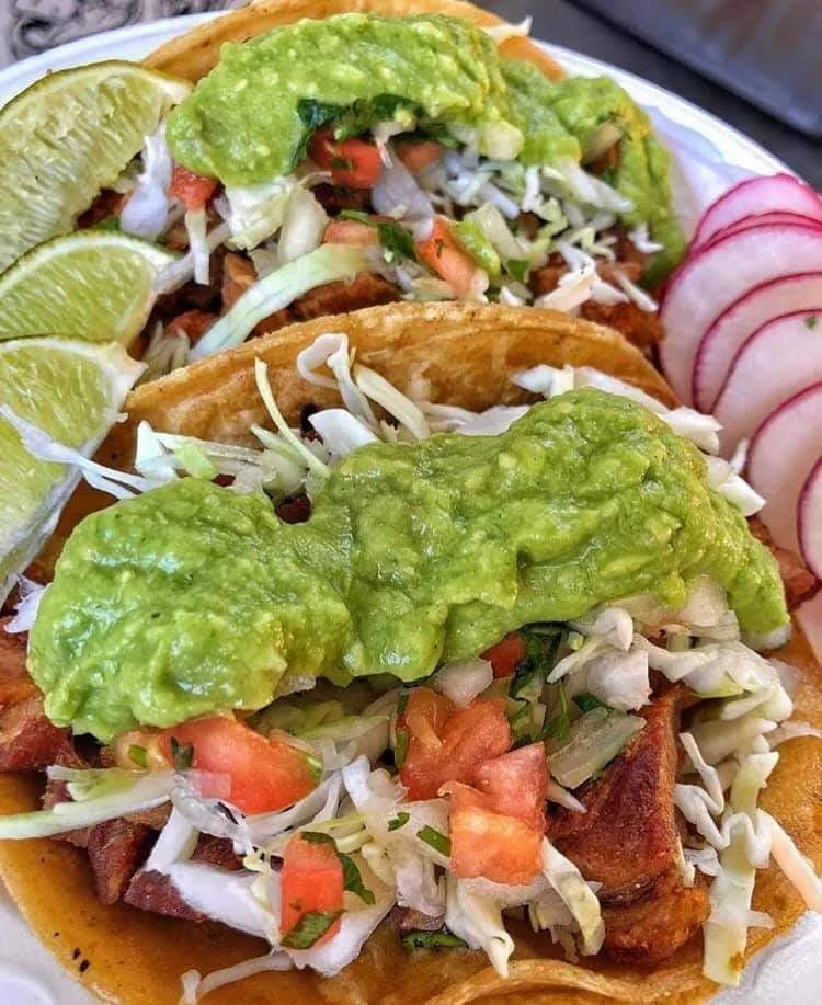 Tacos topped with guacamole, cabbage and tomato